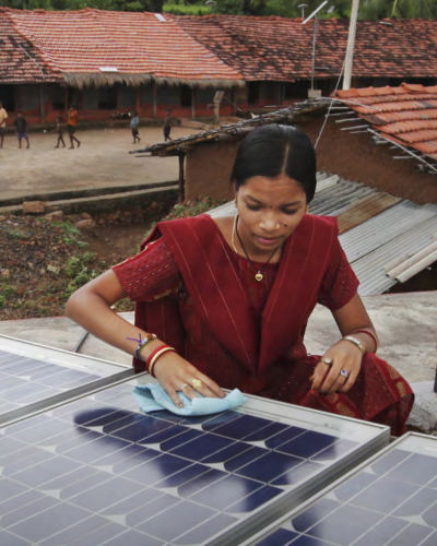 Person cleaning a solar panel installation on a rooftop in a rural community