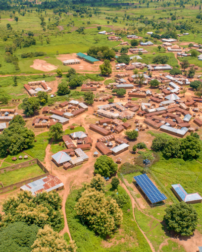 Aerial view of a rural community surrounded by greenery, with homes, roads, and a solar-powered mini-grid installation visible near the village center.