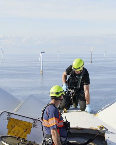 Credit: Ørsted Technicians work atop an offshore wind turbine, with wind turbines visible across the sea.
